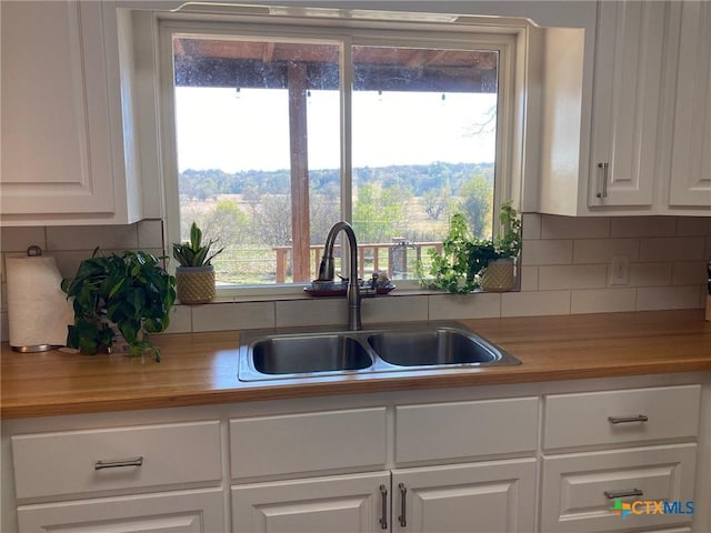 kitchen featuring decorative backsplash, white cabinetry, sink, and wooden counters