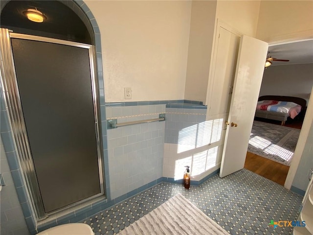 bathroom featuring ceiling fan, a shower with shower door, and tile walls