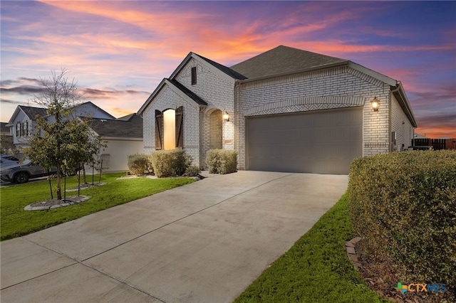 french country style house featuring brick siding, a yard, a shingled roof, a garage, and driveway