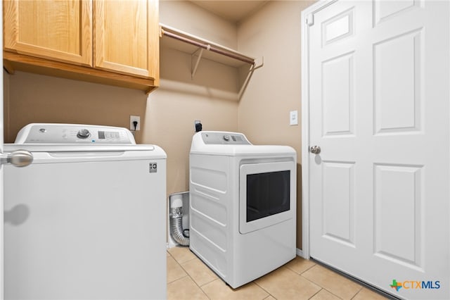 laundry room with washing machine and clothes dryer, light tile patterned floors, and cabinets