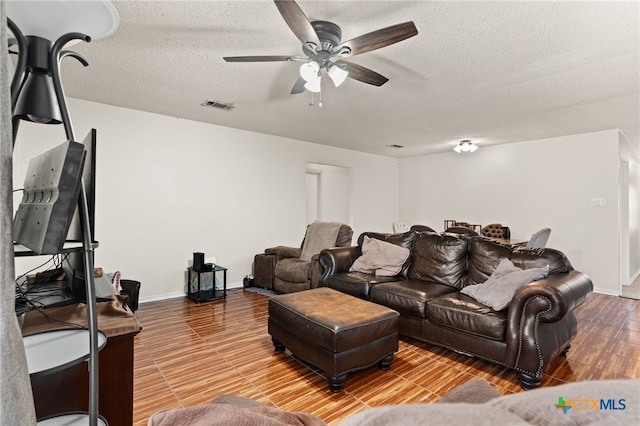 living room featuring a textured ceiling, baseboards, visible vents, and ceiling fan