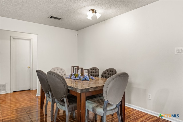 dining space with baseboards, wood finished floors, visible vents, and a textured ceiling