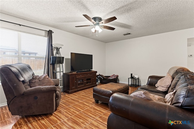 living room featuring a ceiling fan, visible vents, and a textured ceiling