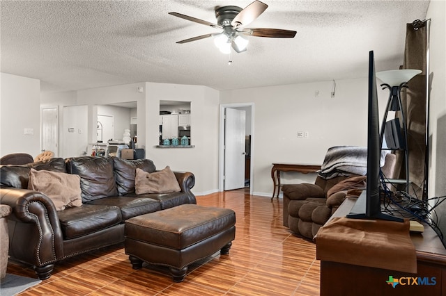 living room featuring light wood-type flooring, a ceiling fan, baseboards, and a textured ceiling