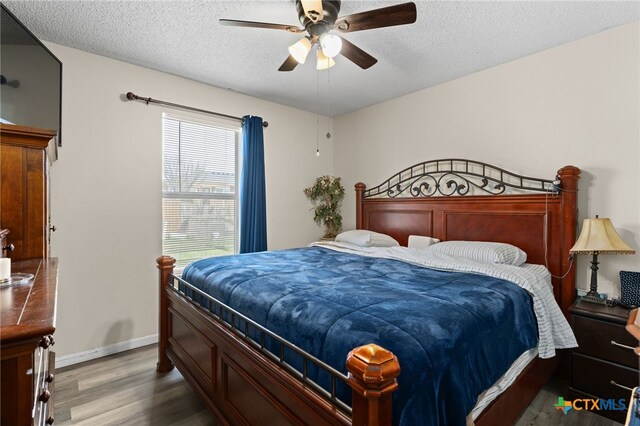 bedroom with a ceiling fan, wood finished floors, baseboards, and a textured ceiling