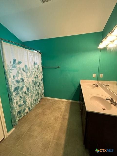 bathroom with double vanity, a sink, baseboards, and lofted ceiling