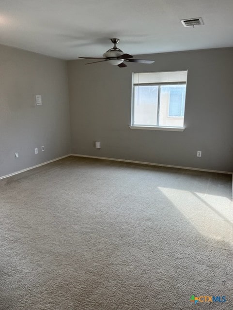 carpeted spare room with visible vents, baseboards, and ceiling fan