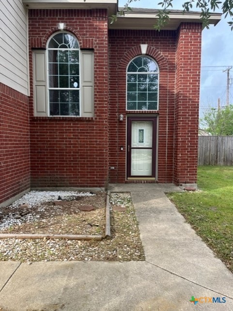 view of exterior entry with fence and brick siding