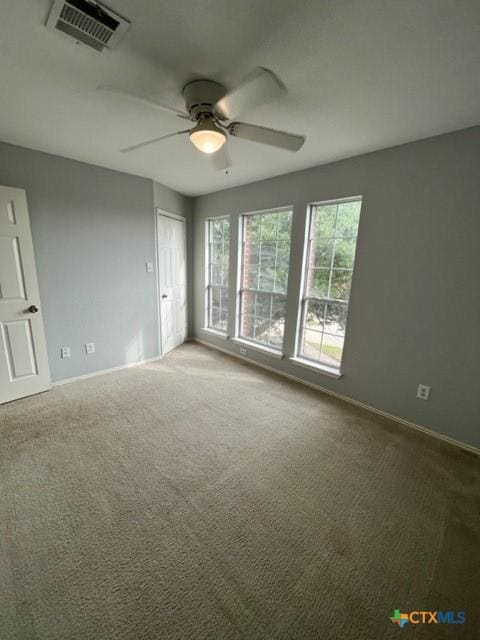 carpeted spare room with visible vents, a ceiling fan, and baseboards