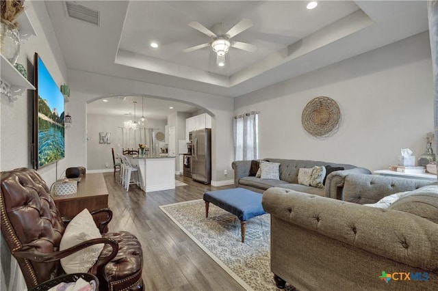 living room with dark hardwood / wood-style floors, a raised ceiling, and ceiling fan with notable chandelier