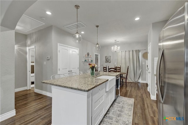 kitchen with a kitchen island with sink, sink, decorative light fixtures, white cabinetry, and stainless steel refrigerator