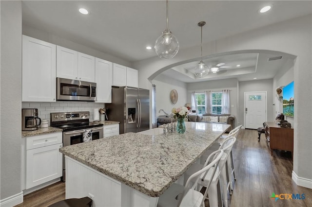 kitchen featuring stainless steel appliances, white cabinetry, hanging light fixtures, and a tray ceiling