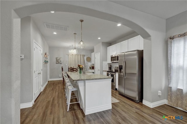 kitchen featuring light stone countertops, stainless steel appliances, decorative light fixtures, white cabinets, and a kitchen island