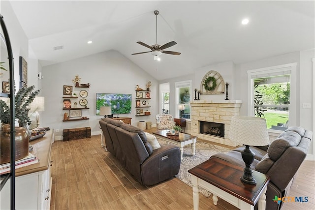 living room featuring light wood-style floors, a ceiling fan, a wealth of natural light, and a stone fireplace