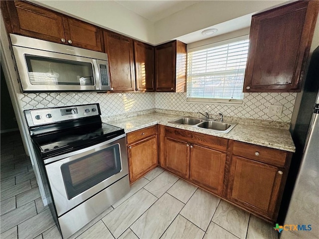 kitchen featuring appliances with stainless steel finishes, backsplash, light stone counters, and sink