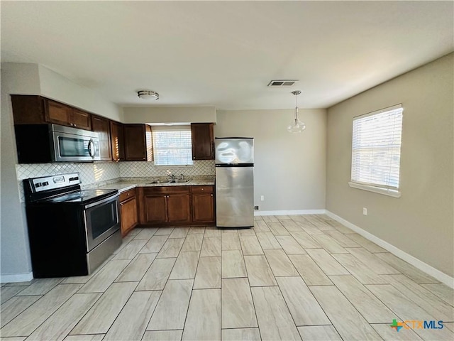 kitchen with appliances with stainless steel finishes, decorative light fixtures, a wealth of natural light, and sink