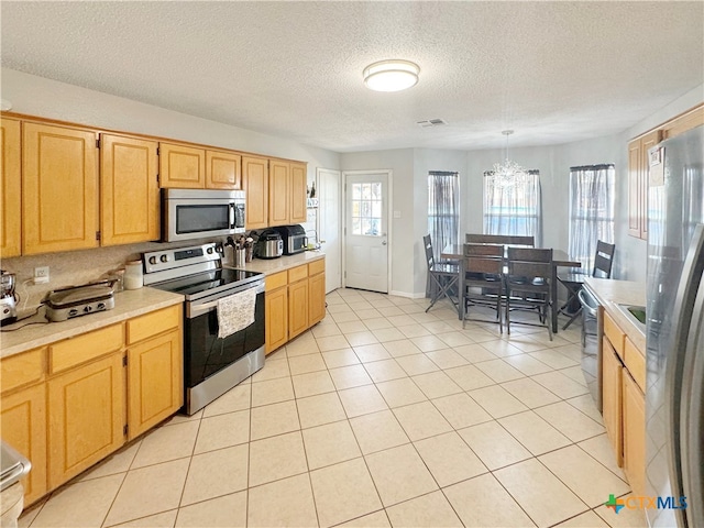 kitchen featuring stainless steel appliances, a textured ceiling, light tile patterned floors, and decorative light fixtures