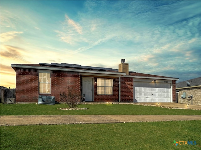 ranch-style home featuring a garage, a yard, and solar panels