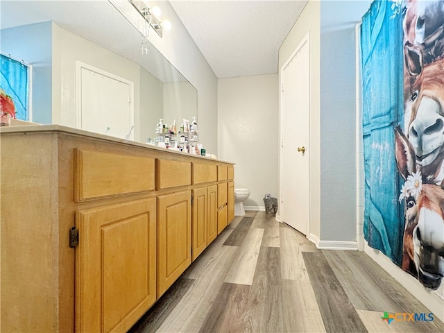 bathroom with a shower with shower curtain, a textured ceiling, wood-type flooring, vanity, and toilet