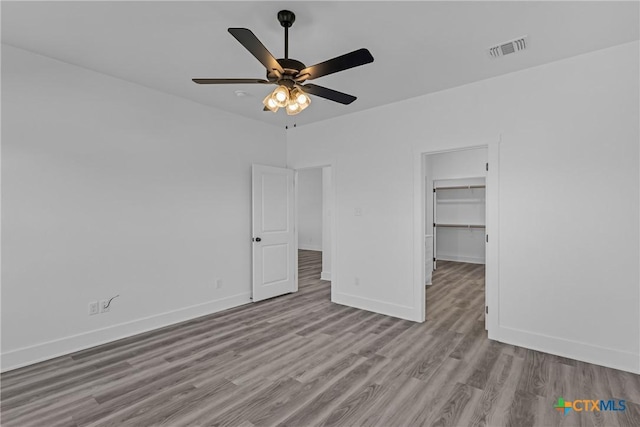 unfurnished bedroom featuring a closet, a walk in closet, light hardwood / wood-style floors, and ceiling fan