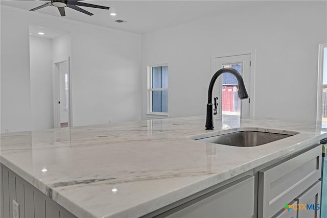 kitchen featuring light stone counters, ceiling fan, and sink