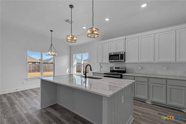 kitchen with sink, dark wood-type flooring, light stone counters, a center island with sink, and appliances with stainless steel finishes