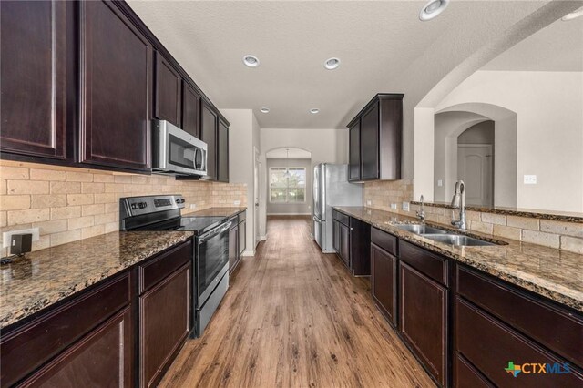 4703 Prewitt Ranch Rd, Killeen, TX 76549 - kitchen with appliances with stainless steel finishes, a sink, dark stone countertops, light wood-type flooring, and arched walkways