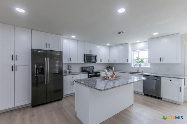 kitchen with appliances with stainless steel finishes, a sink, white cabinetry, and light stone countertops