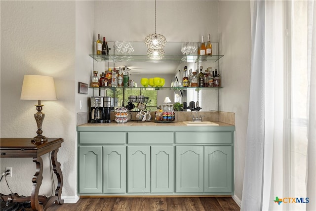 bar featuring dark wood-type flooring, sink, hanging light fixtures, and green cabinets