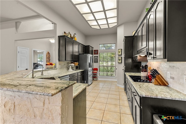 kitchen featuring sink, kitchen peninsula, stainless steel refrigerator with ice dispenser, light stone countertops, and backsplash