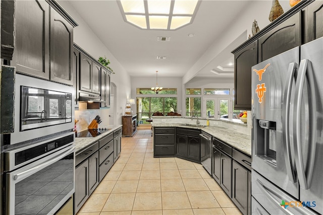 kitchen featuring sink, light stone counters, appliances with stainless steel finishes, light tile patterned floors, and hanging light fixtures