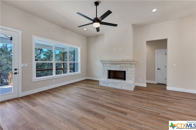 unfurnished living room with a stone fireplace, a wealth of natural light, wood-type flooring, and ceiling fan