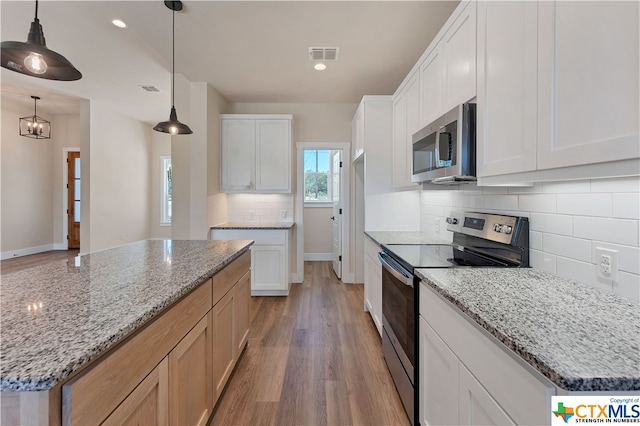 kitchen featuring white cabinets, hanging light fixtures, light stone countertops, light wood-type flooring, and appliances with stainless steel finishes