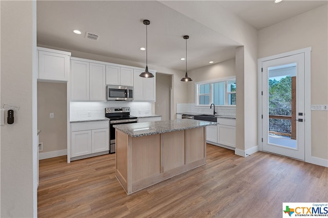 kitchen with stainless steel appliances, light stone counters, white cabinets, a kitchen island, and pendant lighting