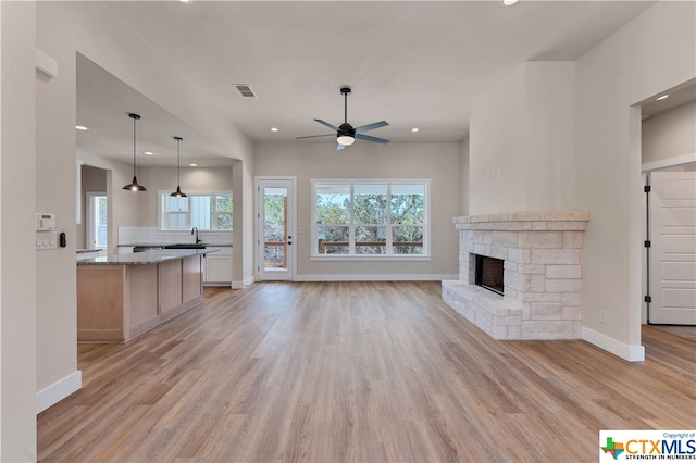 unfurnished living room with a stone fireplace, light wood-type flooring, sink, and ceiling fan