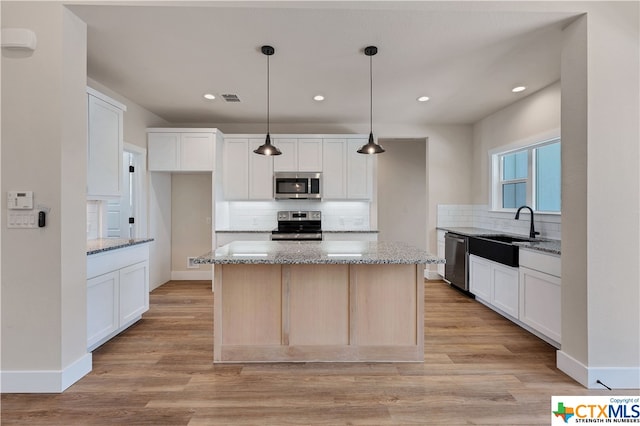 kitchen featuring sink, appliances with stainless steel finishes, light stone countertops, a center island, and white cabinets