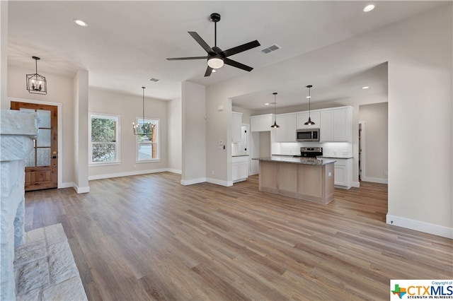 kitchen with a kitchen island with sink, appliances with stainless steel finishes, decorative light fixtures, white cabinets, and light hardwood / wood-style flooring