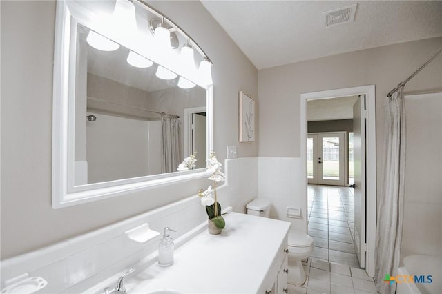 full bathroom featuring visible vents, toilet, wainscoting, french doors, and tile walls