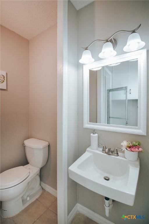 half bath featuring tile patterned floors, toilet, baseboards, and a sink