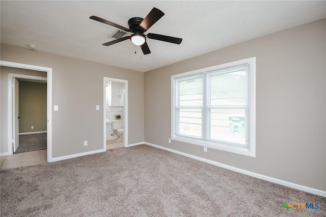 unfurnished bedroom with a ceiling fan, baseboards, ensuite bath, a textured ceiling, and light carpet