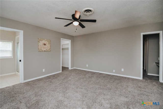 unfurnished bedroom featuring visible vents, a walk in closet, baseboards, carpet floors, and a textured ceiling