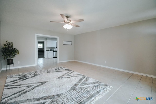 empty room featuring light tile patterned floors, a ceiling fan, and baseboards