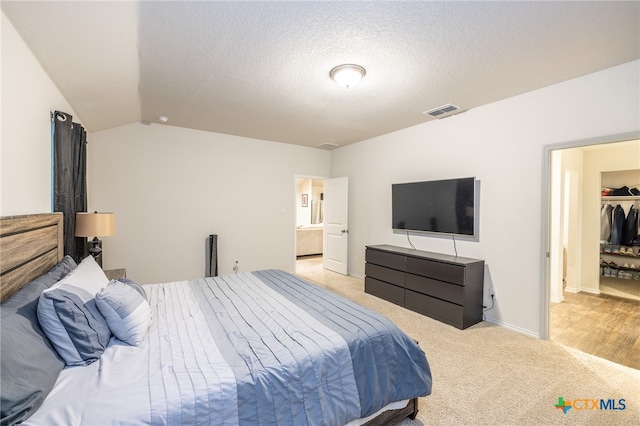 carpeted bedroom featuring ensuite bath, a spacious closet, a textured ceiling, vaulted ceiling, and a closet