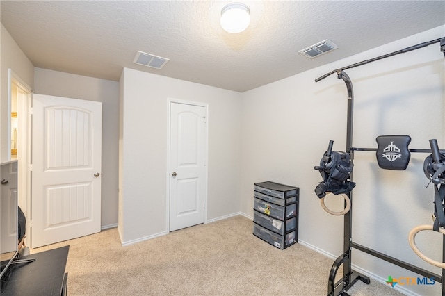 exercise area with light colored carpet and a textured ceiling