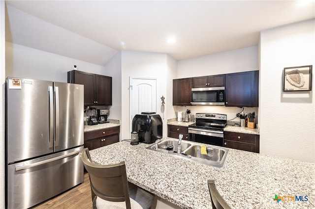 kitchen featuring appliances with stainless steel finishes, dark brown cabinets, sink, light hardwood / wood-style flooring, and a breakfast bar area