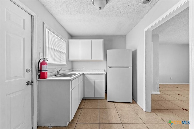 kitchen featuring white refrigerator, light tile patterned floors, sink, and white cabinets