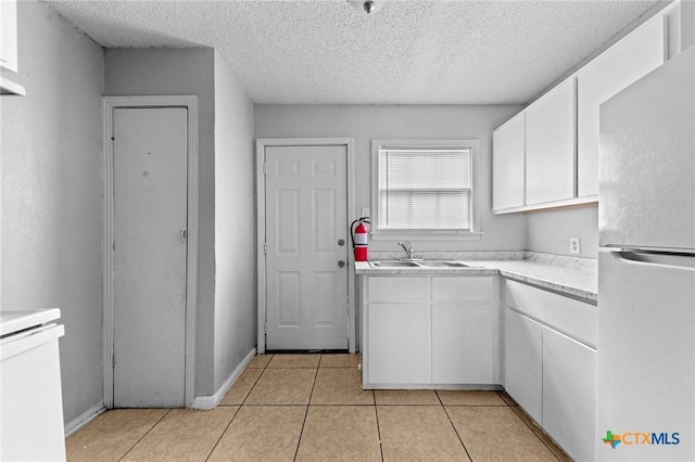 kitchen with light tile patterned flooring, sink, white cabinets, white fridge, and a textured ceiling