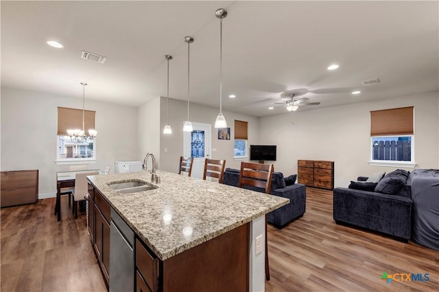 kitchen featuring sink, hanging light fixtures, light stone counters, a center island with sink, and light wood-type flooring