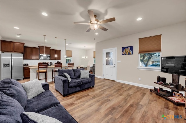 living room featuring ceiling fan with notable chandelier and light hardwood / wood-style floors