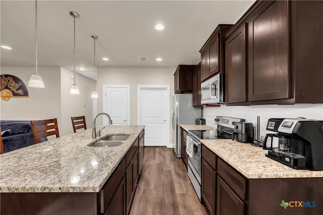 kitchen featuring dark wood-type flooring, sink, hanging light fixtures, stainless steel appliances, and a kitchen island with sink